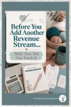 Pinterest pin showing a cozy handmade business desk with yarn, calculator, income tracker, receipts, mug, and text about tracking a new revenue stream before adding it.